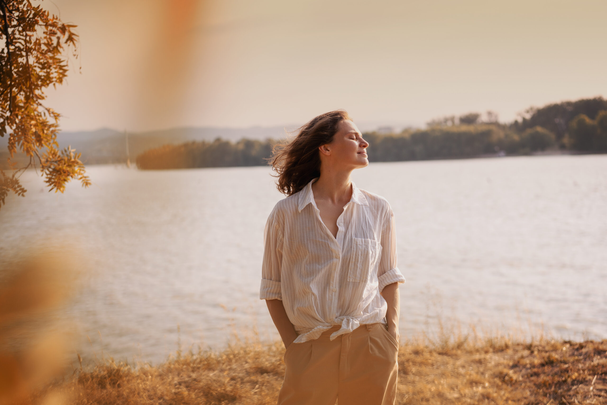 Beautiful young relaxed woman in white blouse enjoying nature breathing fresh air meditating on the river on an autumn